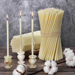 Pode incluir: Três velas brancas com chamas em castiçais de mármore e um pacote de velas de pavio branco amarradas com barbante.