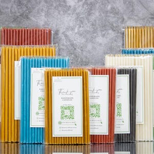 May include: Assortment of handmade candles in various colours, including green, purple, yellow, orange, blue, red, black, white, and gold. The candles are packaged in clear plastic and labelled with a QR code and the text "Thank you for choosing handmade candles".