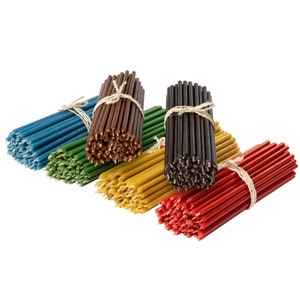 May include: A selection of colourful taper candle bundles. The bundles are in shades of blue, green, brown, yellow, black, and red, tied with twine. The candles are arranged in a row, showcasing their vibrant colours and textures.