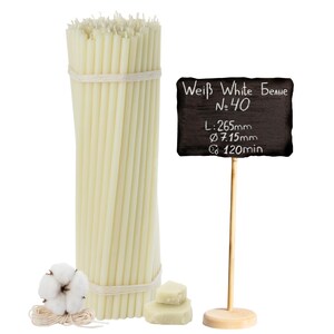 Puede incluir: Un paquete de velas cónicas de color marfil atadas con hilo, junto a una pequeña pizarra sobre un soporte de madera. El letrero dice "Weiß White Белые No. 40" con medidas: L: 265mm, Ø 7.15mm, y tiempo de combustión 120min. También se muestra algodón y cera.