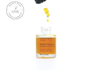 May include: A clear glass bottle of Bloom Facial Oil with a dropper dispensing a yellow liquid. The label reads "love & light BOTANICALS" and "BLOOM FACIAL OIL botanical retinol alternative". The bottle contains 18 ml or .6 fl oz of product.