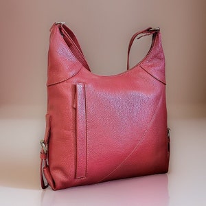 May include: A red leather shoulder bag with a flap closure and a zippered pocket on the front. The bag has a textured leather finish and a silver-toned hardware.