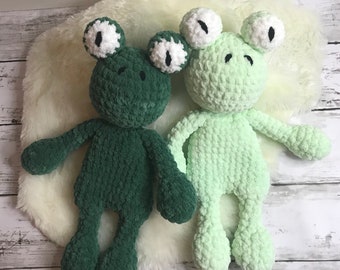 Op de afbeelding: Twee gehaakte kikker knuffels, één groen en één lichtgroen, met witte ogen en zwarte pupillen. De kikkers zitten op een wit, pluche oppervlak.