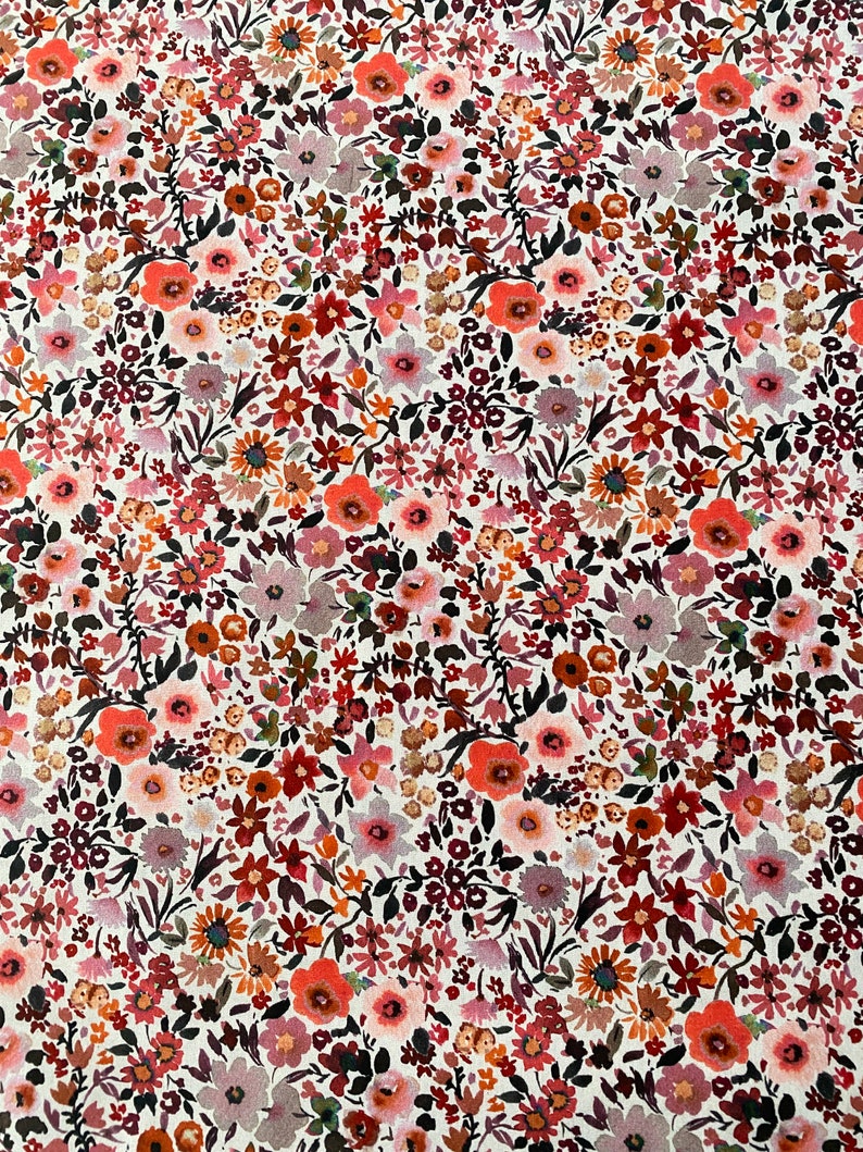 May include: A close-up of a floral fabric with a white background. The fabric is densely covered with small flowers in shades of red, orange, pink, and purple, with green leaves. The overall effect is a vibrant, colorful pattern.