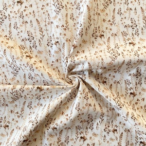 Könnte beinhalten: Weißer Stoff mit braunem Blumenmuster. Der Stoff ist spiralförmig gefaltet und zeigt das Muster im Detail.