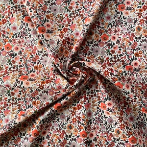 May include: A close-up of a floral fabric featuring a dense pattern of small flowers in shades of red, orange, pink, and brown. The fabric is white with a slight sheen, and the flowers are arranged closely together.
