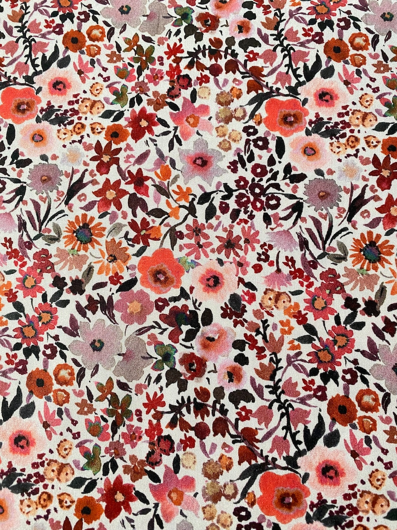 May include: A fabric with a detailed floral print. The pattern is composed of numerous small flowers in hues of red, orange, pink, and purple, set against a white backdrop. The flowers are of different sizes and shapes, creating a textured and visually rich surface.