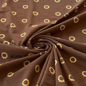 May include: Brown fabric featuring a repeating pattern of yellow sunflowers. The fabric is gathered and folded, creating a textured appearance. The sunflowers have black centres and are evenly spaced across the material.