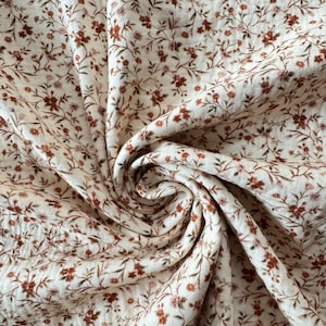 Könnte beinhalten: Nahaufnahme eines weißen Stoffes mit einem kleinen, braunen Blumenmuster. Der Stoff ist zerknittert und hat eine strukturierte Oberfläche.