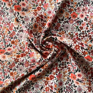 May include: Close-up of a floral fabric. The fabric is covered in a dense pattern of small flowers in shades of red, pink, orange, and brown against a cream background. The fabric is slightly creased, showing its texture and folds.
