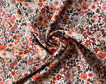 May include: Close-up of a fabric with a floral pattern. The fabric features a dense arrangement of small flowers in shades of red, pink, orange, and brown against a cream-colored background. The fabric is slightly wrinkled, showing the texture and folds.
