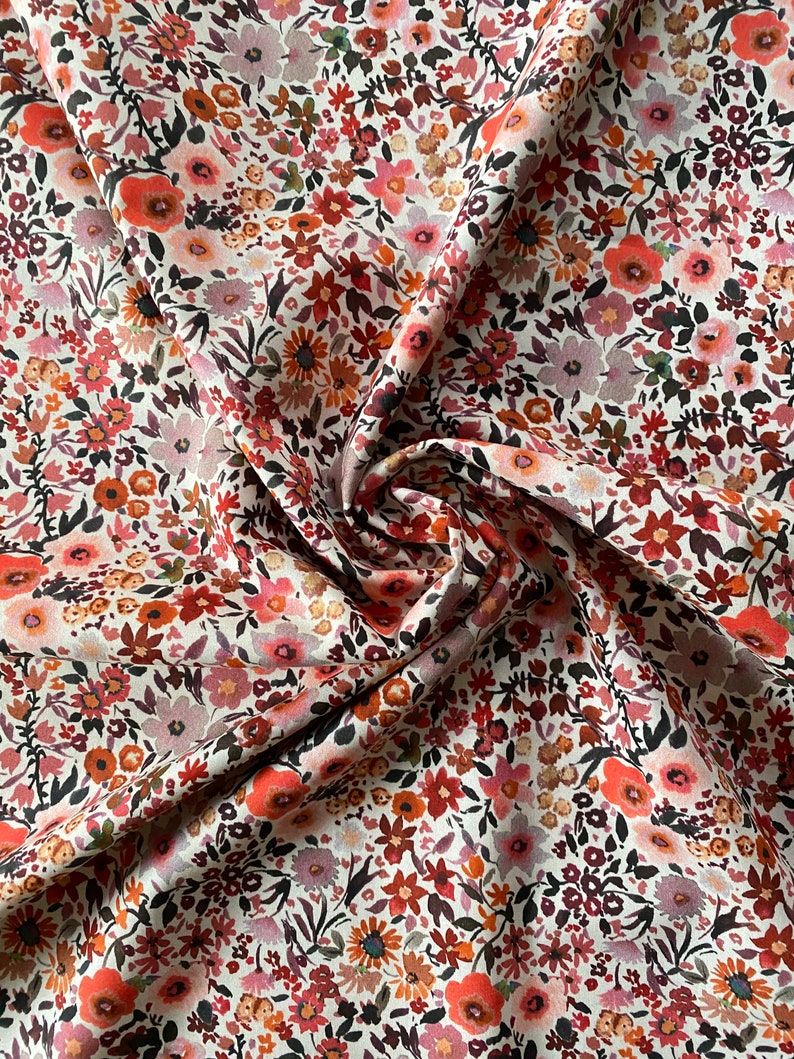 May include: Close-up of a floral fabric. The fabric is covered in a dense pattern of small flowers in shades of red, pink, orange, and brown against a cream background. The fabric is slightly creased, showing its texture and folds.