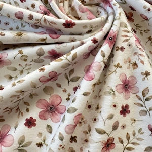 Könnte beinhalten: Nahaufnahme eines weißen Stoffes mit floralem Muster. Das Design zeigt rosa und burgunderfarbene Blumen sowie grüne und braune Blätter und Stiele. Der Stoff ist weich und scheint drapiert zu sein.