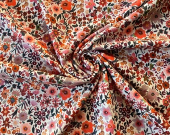 May include: Close-up of a fabric with a dense floral pattern. The design features a variety of small flowers in shades of orange, pink, and burgundy, set against a cream-colored background. The fabric is gathered, showing the texture and folds.