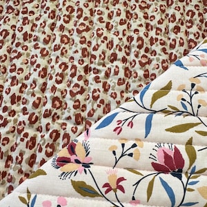 Peut inclure: Tissu matelassé avec deux motifs distincts. Un côté présente un fond crème avec des taches de léopard marron. L'autre côté affiche un motif floral avec des fleurs roses, rouges et bleues sur fond crème. Le tissu est cousu avec des lignes verticales.