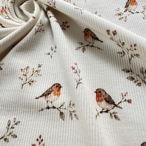 May include: A cream-colored ribbed fabric featuring a repeating pattern of small brown and orange robins perched on thin branches with delicate leaves and tiny red berries. The material is draped to show the texture and the print design clearly.