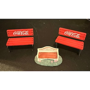 以下が含まれることがあります： 背もたれに白い文字でDrink Coca-Colaと書かれた2つの赤いミニチュアパークベンチと、白いフレーム、茶色の座面、緑の草と小さなピンクの花を模したテクスチャーの土台を持つ、より小さな装飾用ベンチ。