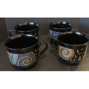 Pode incluir: Quatro canecas de cerâmica preta com alças. Cada caneca apresenta um design único com fundo preto e um padrão de redemoinhos e traços pintados em tons de azul, cinza e bege. As canecas estão dispostas sobre uma superfície escura.
