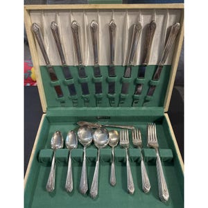 May include: A silver-plated flatware set in a wooden storage case with green velvet lining. The set includes eight knives with ornate handles, five spoons of varying sizes, two forks, and one serving piece, all featuring a classic embossed pattern.