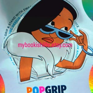 May include: A PopGrip featuring a cartoon image of a woman with black hair, blue sunglasses, and a white fur-trimmed collar. The PopGrip has the text "POPGRIP" in orange and pink. The Etsy shop name "mybookishlife.etsy.com" is also visible.