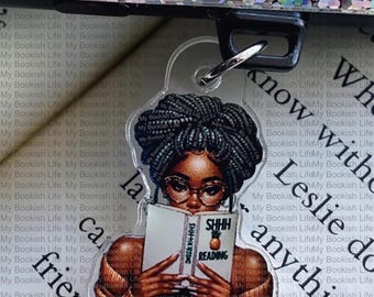 Puede incluir: Llavero acrílico transparente que presenta a una mujer negra con gafas leyendo un libro con "SHHH READING" en la portada. El llavero tiene un cierre plateado y las palabras "My Bookish Life" se repiten en el fondo.