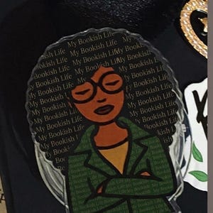 Könnte beinhalten: Ein klarer Acryl-Pin mit einer Cartoon-Illustration einer Frau mit Brille und grüner Jacke. Der Pin ist mit den Worten "My Bookish Life" verziert, was ihn zu einem Accessoire zum Thema Buch macht.