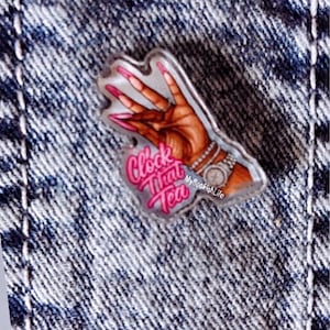 May include: An acrylic pin featuring a hand with long pink nails making a gesture, wearing a silver watch and bracelets. The text "Clock That Tea" is printed in bright pink script, with "MyBookishLife" in smaller white text below the watch.