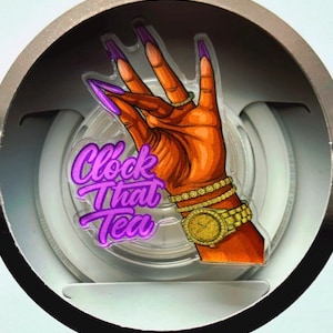 May include: A MagSafe charger with a graphic of a hand with long purple nails, a gold watch, and bracelets. The text "Clock That Tea" is in purple. The charger is in a silver circular frame.