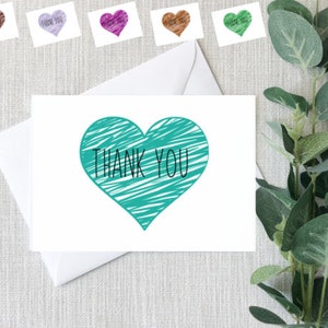 May include: A white card with a teal blue heart drawn on it. The heart has a scribbled pattern and the words "THANK YOU" are written inside the heart.