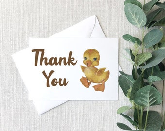 May include: A white thank you card with brown text that says "Thank You". A yellow duckling with brown eyes and orange feet is on the right side of the card.