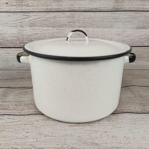 May include: White enamelware pot with a lid and black trim. The pot has a speckled design and black handles. The lid has a black handle. The pot is likely used for cooking and is a vintage kitchen item.