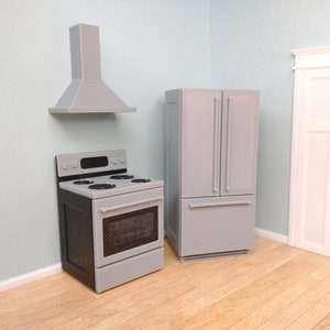 Peut inclure: Un ensemble de cuisine miniature avec un réfrigérateur gris, une cuisinière grise avec un four et une hotte aspirante grise. L'ensemble est posé sur un sol en bois clair.