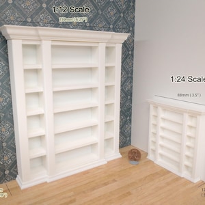 May include: Two white miniature bookshelves, one larger than the other. The larger bookshelf is 6.25 inches tall and 7 inches wide. The smaller bookshelf is 3.5 inches tall and 3.5 inches wide. Both bookshelves have five shelves each.