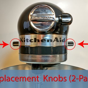Puede incluir: Dos perillas de reemplazo negras para una batidora de pie KitchenAid. Las perillas están ubicadas a cada lado del logotipo de KitchenAid en la cabeza de la batidora.