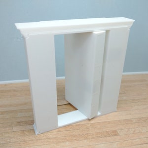 May include: A white, rectangular, decorative door frame with a single door that is open. The door frame is made of a lightweight material, possibly plastic or foam.