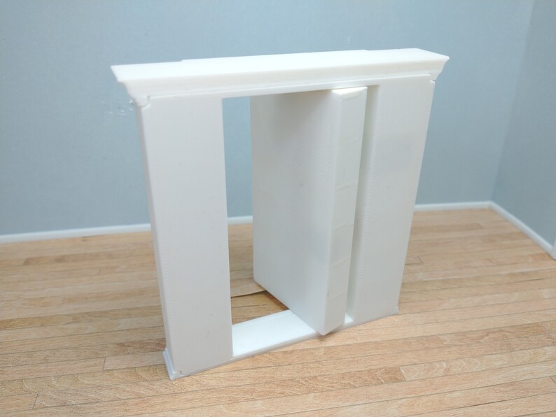 May include: A white, rectangular, decorative door frame with a single door that is open. The door frame is made of a lightweight material, possibly plastic or foam.