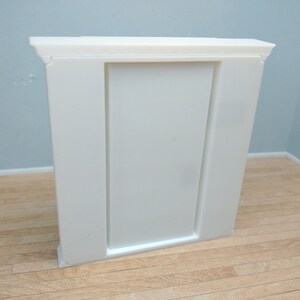 May include: White painted wooden fireplace mantel with a rectangular opening. The mantel has a simple design with a flat top and a slightly raised base.