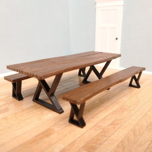 May include: A miniature wooden picnic table set with two benches. The table and benches have a brown wood finish and black metal legs.