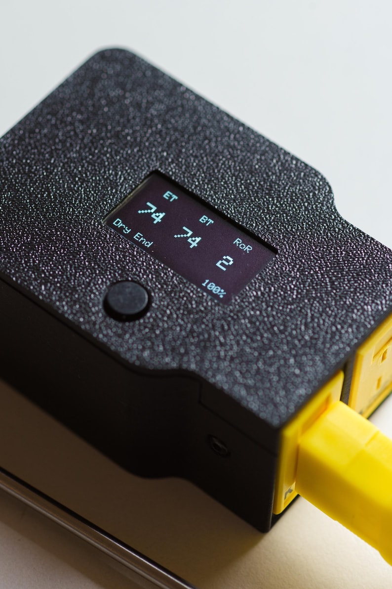 Puede incluir: Primer plano de un dispositivo electr&oacute;nico negro con una superficie texturizada. El dispositivo tiene una peque&ntilde;a pantalla que muestra n&uacute;meros y texto, incluyendo "ET", "BT" y "RoR". Un enchufe amarillo se extiende desde el lateral. Un bot&oacute;n es visible.