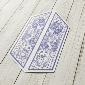 May include: A purple and white floral design printed on a sticker. The design features a geometric pattern with a floral motif. The sticker is shaped like a hexagon.