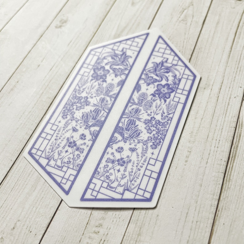 May include: A purple and white floral design printed on a sticker. The design features a geometric pattern with a floral motif. The sticker is shaped like a hexagon.