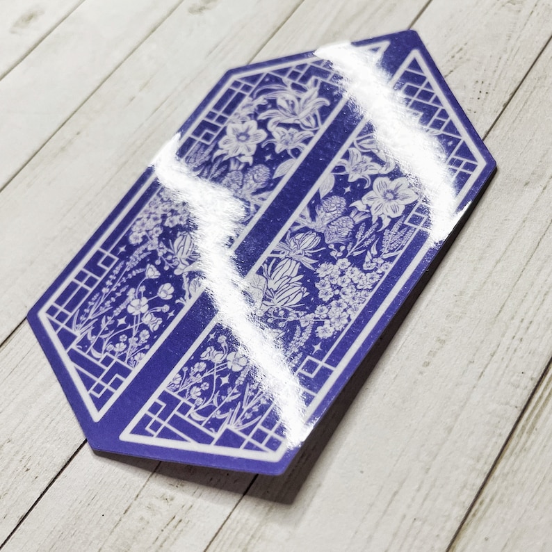 May include: A blue hexagonal sticker with a white floral design. The sticker features a repeating pattern of flowers and leaves within a geometric frame.