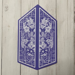 May include: A purple geometric card with a white floral design. The card features a symmetrical design with a floral pattern on each side. The flowers are stylised and include lilies, leaves, and other botanical elements.