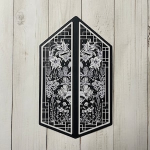 May include: Black and white illustration of a symmetrical design with floral motifs and geometric patterns. The design is framed by a black border and features a repeating pattern of flowers, leaves, and stars.