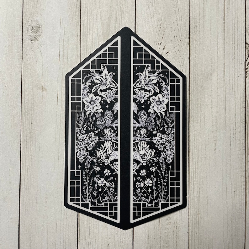 May include: Black and white illustration of a symmetrical design with floral motifs and geometric patterns. The design is framed by a black border and features a repeating pattern of flowers, leaves, and stars.