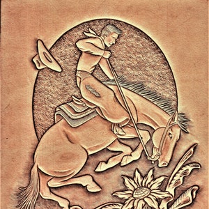 May include: A detailed leather carving shows a cowboy riding a bucking horse. The artwork features a cowboy in chaps, a hat, and a rope, set against a textured background. Floral and scrollwork designs frame the scene, with a sunflower at the bottom.