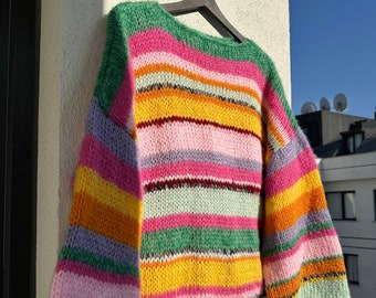 May include: A colorful striped knitted sweater with long sleeves and a wide neckline. The sweater is made with a variety of colors, including pink, green, yellow, orange, and purple.