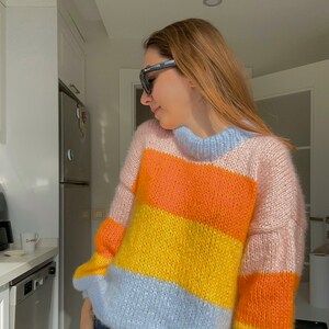 以下が含まれることがあります： ハイネックと長袖のマルチカラーストライプセーター。セーターは柔らかくふわふわした糸でできており、ピンク、オレンジ、イエロー、ライトブルーのストライプが特徴です。