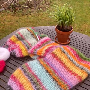 Puede incluir: Una bufanda de punto a rayas de colores con una variedad de colores que incluyen rosa, amarillo, verde y azul. La bufanda est&aacute; sobre una mesa de madera con una planta en maceta en el fondo.