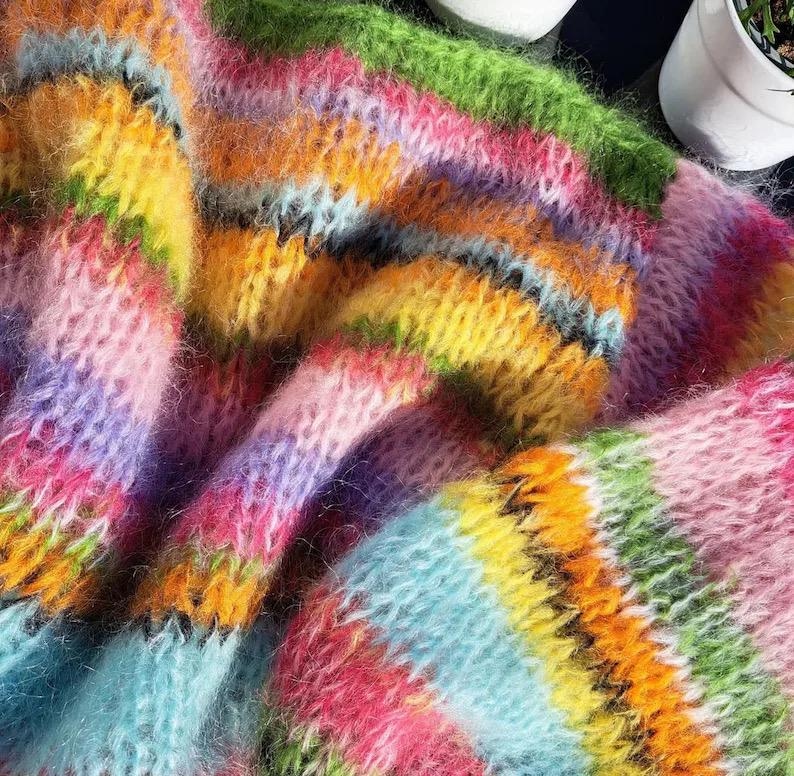 Puede incluir: Un primer plano de un su&eacute;ter de punto de rayas de colores con una textura peluda. El su&eacute;ter est&aacute; hecho de un hilo suave y esponjoso y presenta una variedad de colores brillantes, incluyendo rosa, azul, verde, amarillo y naranja.